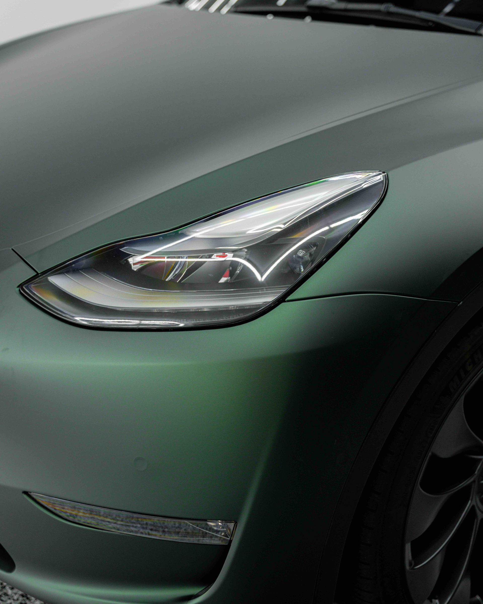 A close up of the headlight of a green tesla model 3.