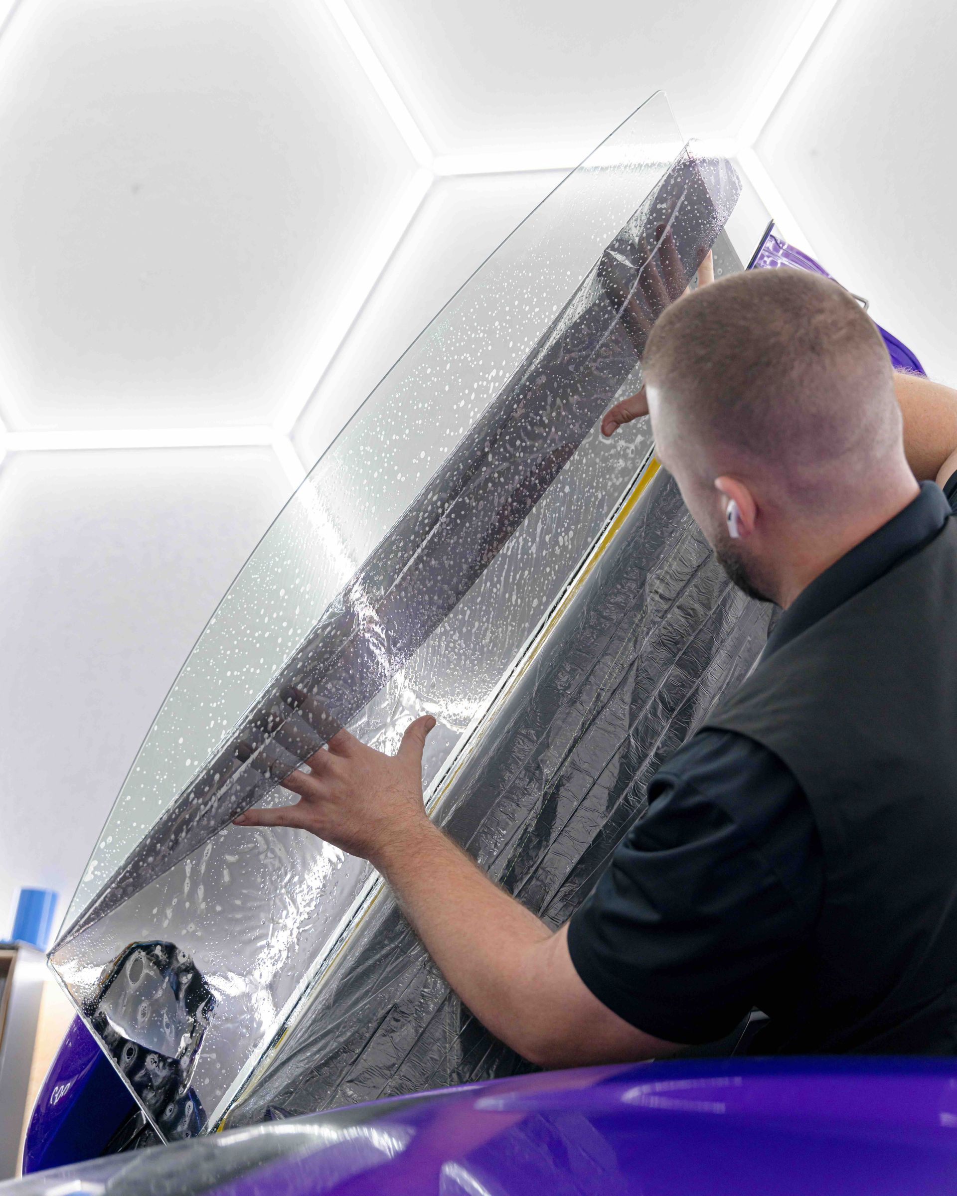 A man is wrapping a purple car with a clear film.