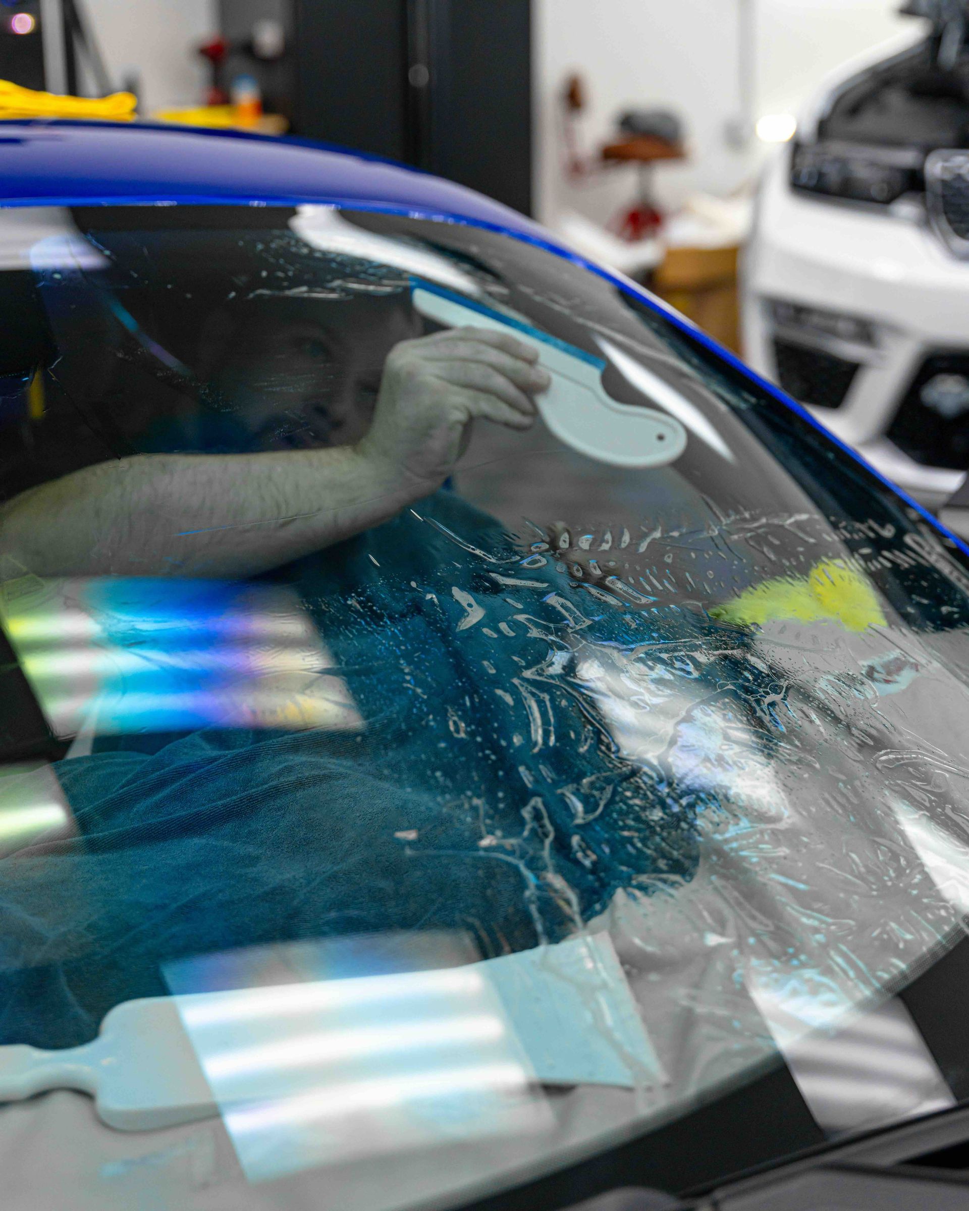 A man is cleaning the windshield of a blue car.