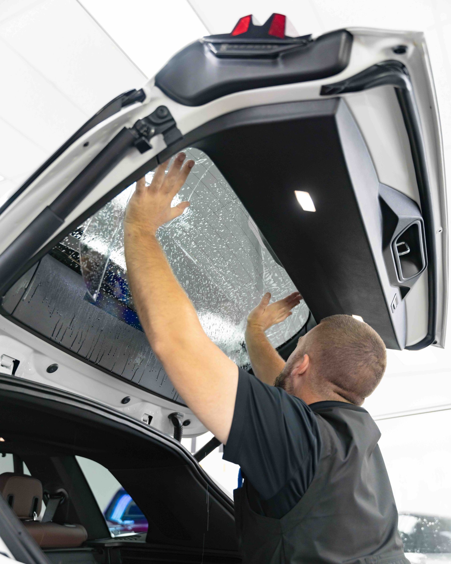 A man is applying tinted glass to the back window of a car