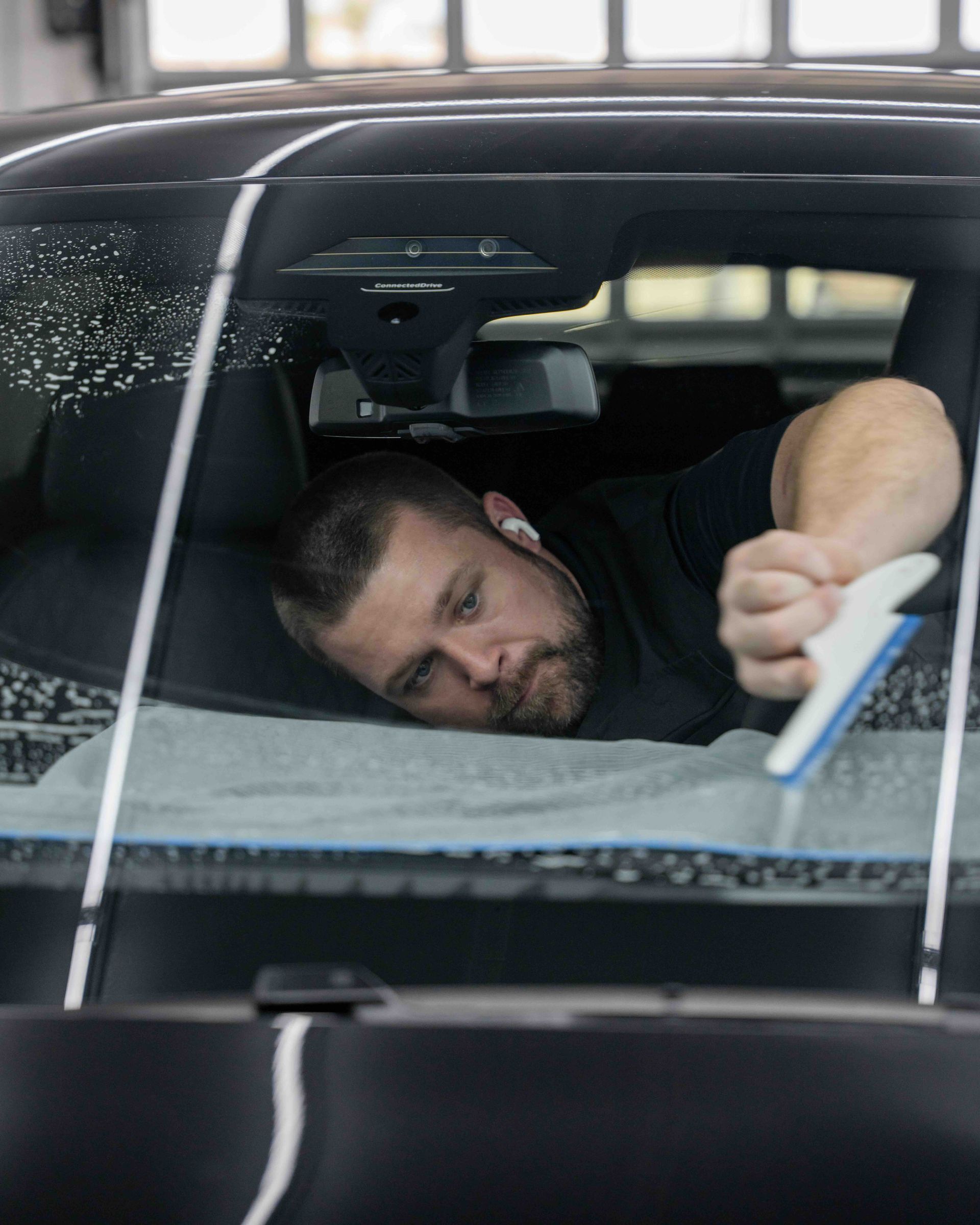 A man is cleaning the windshield of a car with a brush.