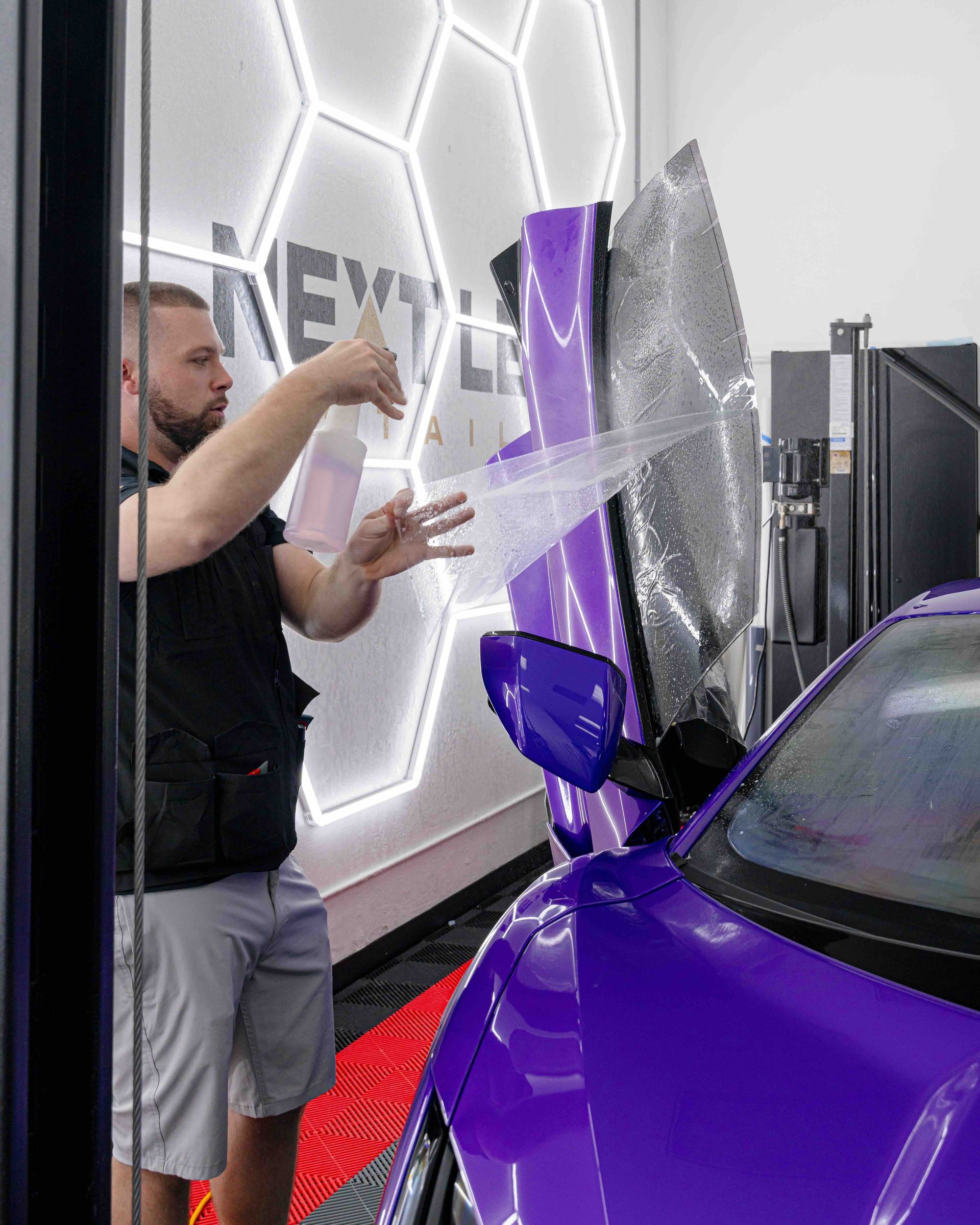 A man is wrapping a purple car in a garage