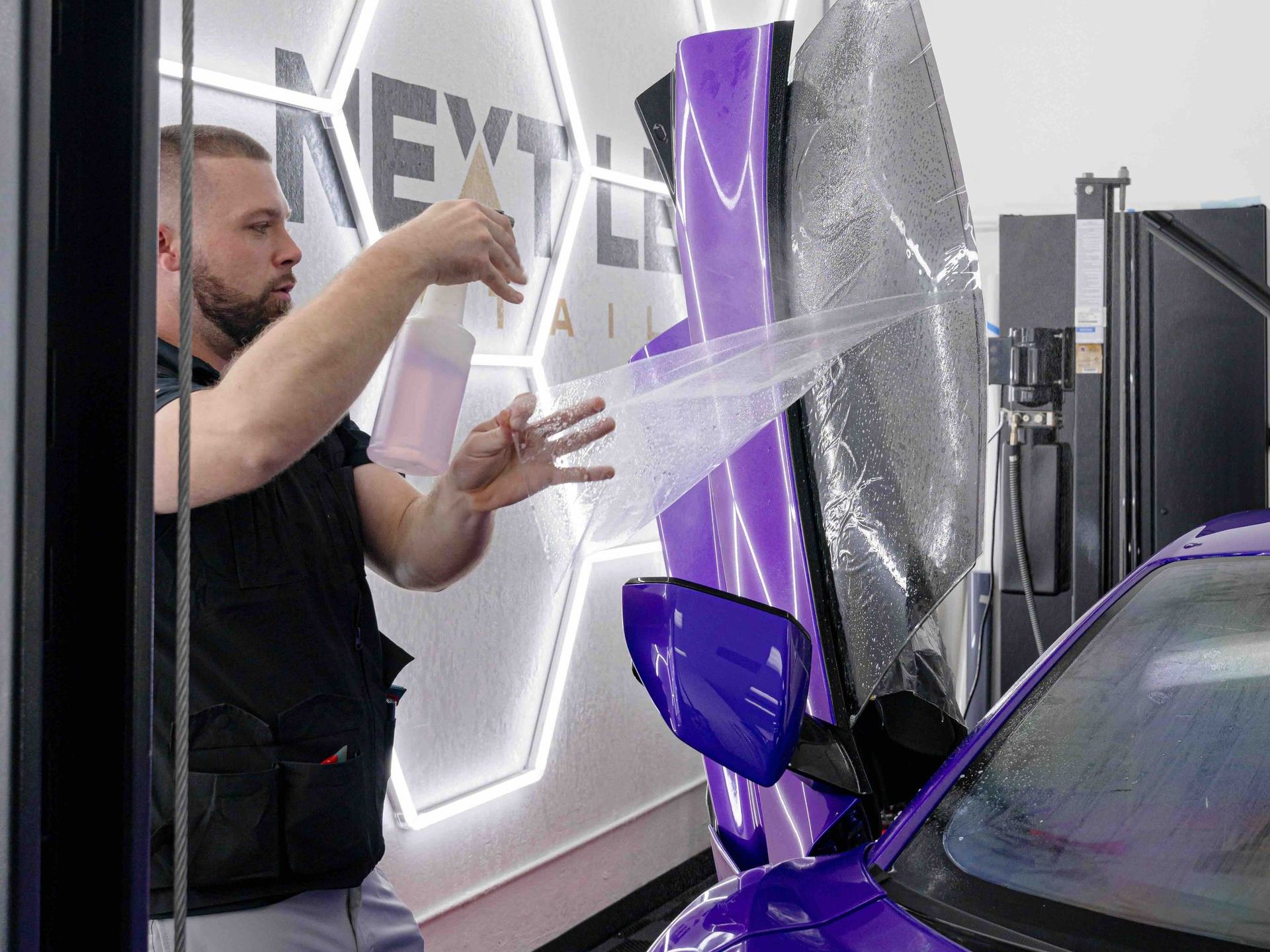 A man is wrapping a purple car with plastic wrap.