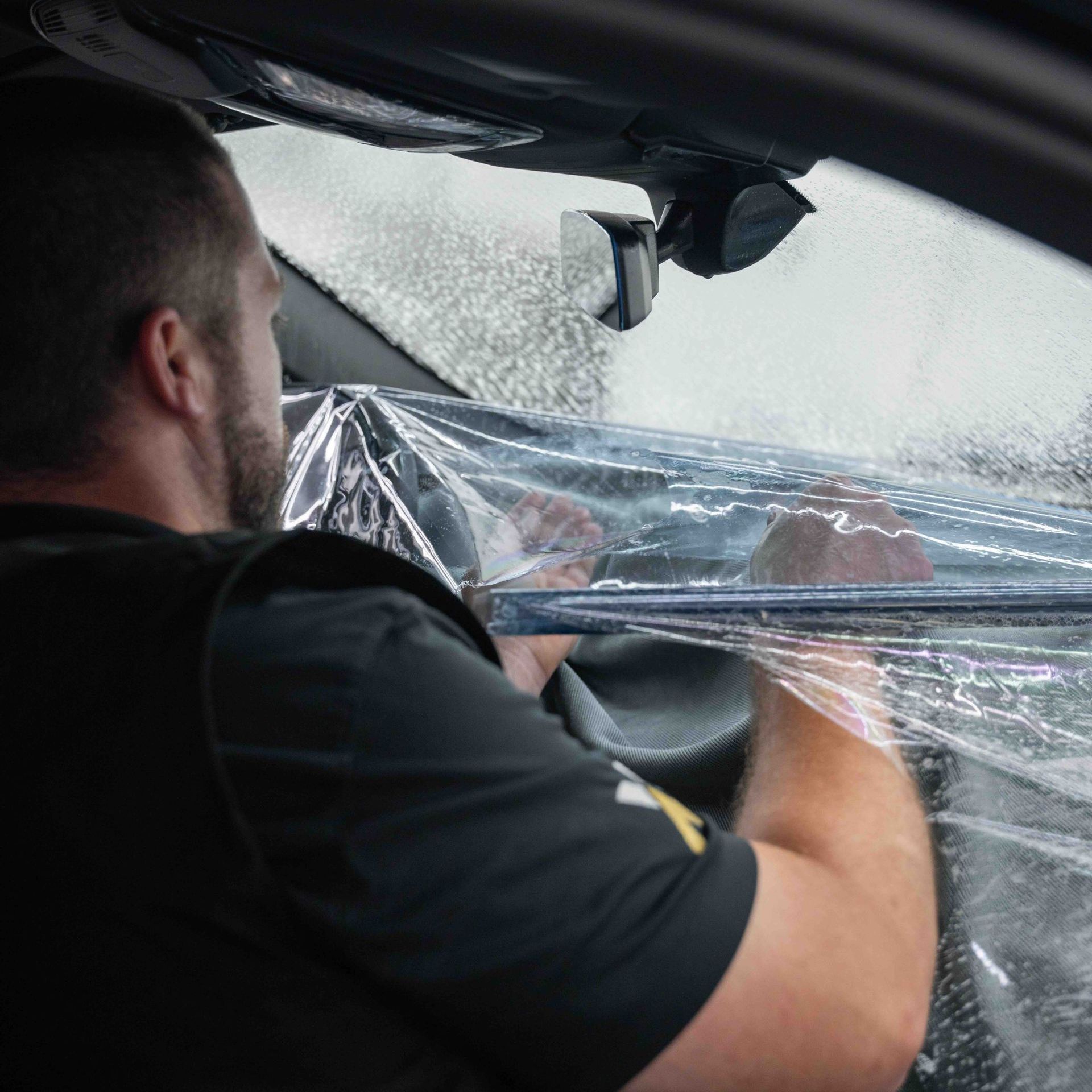 A man is sitting in a car covering his windshield with plastic