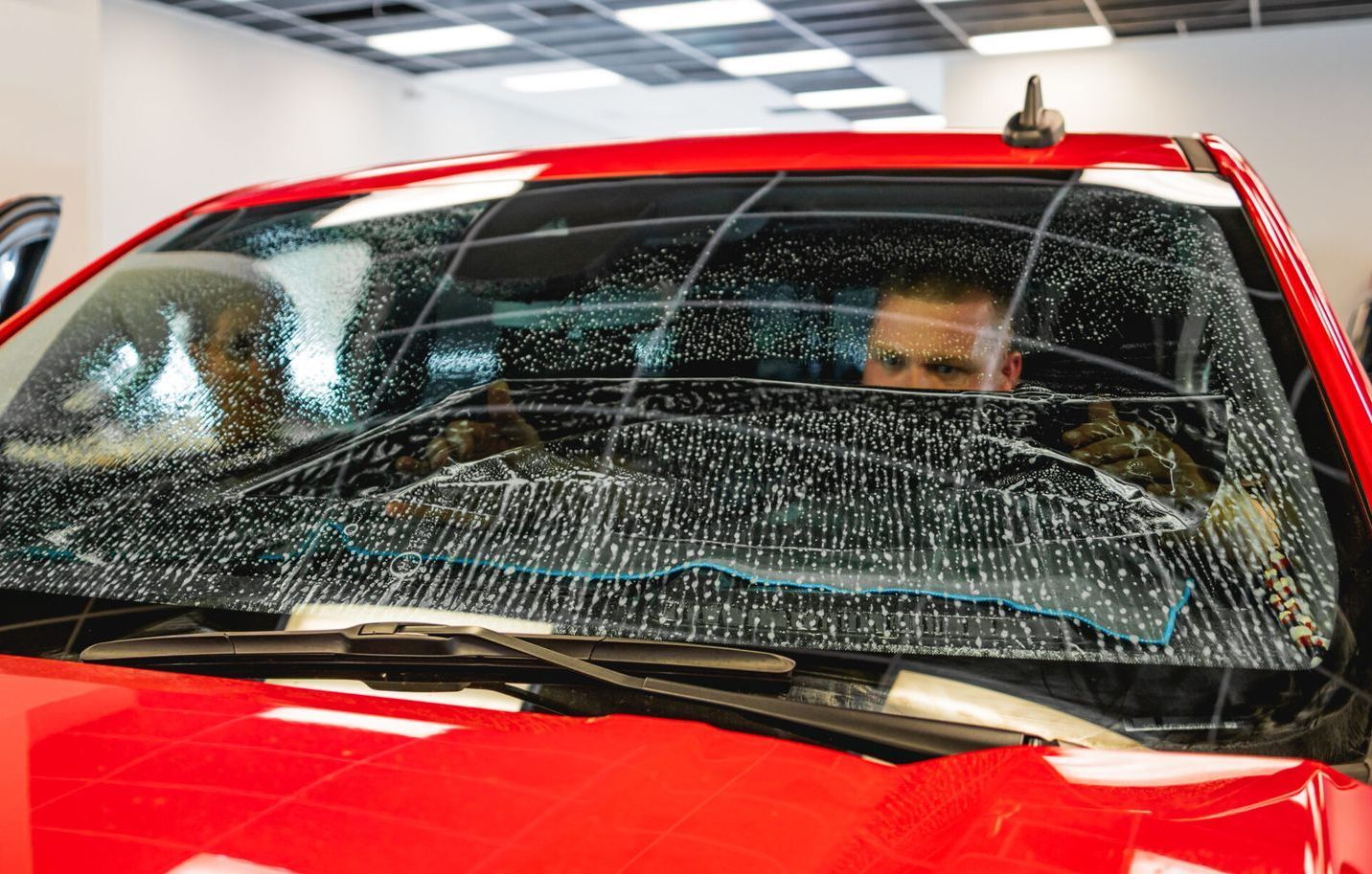 A man is sitting in a red truck with a broken windshield.