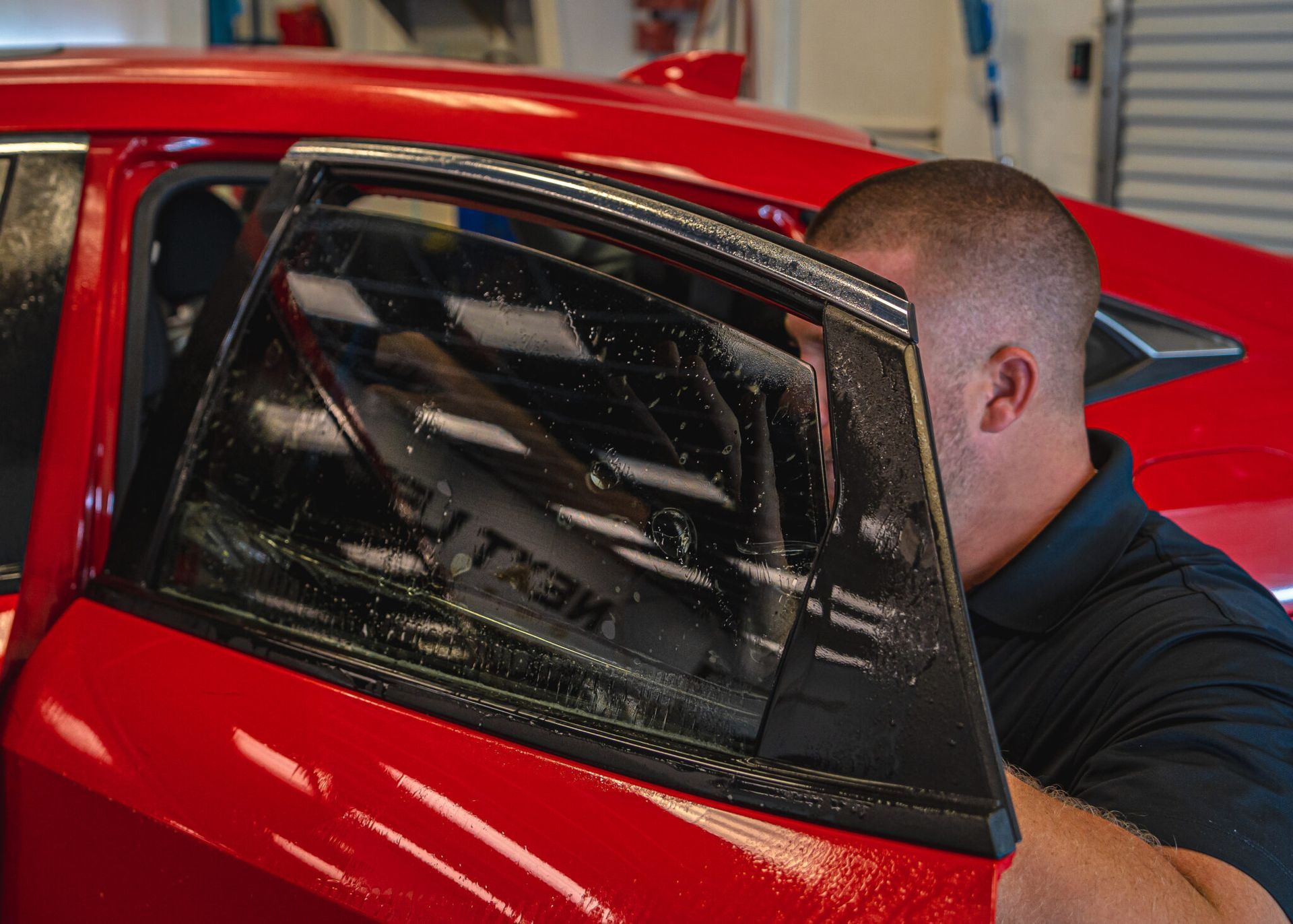 A man is installing window tinting on a red car.