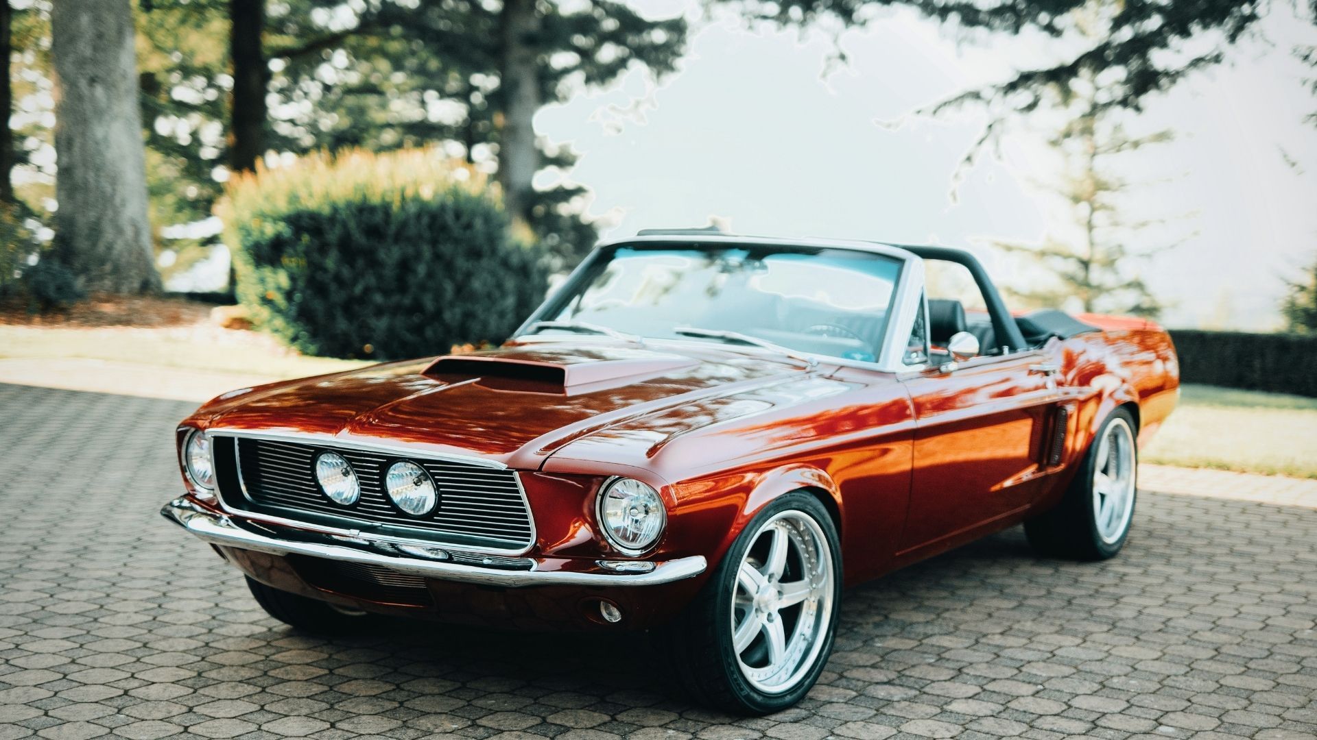 A red mustang convertible is parked in a driveway.