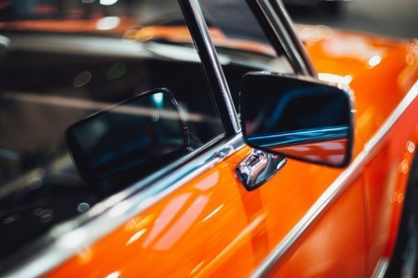 A close up of an orange car with a side mirror