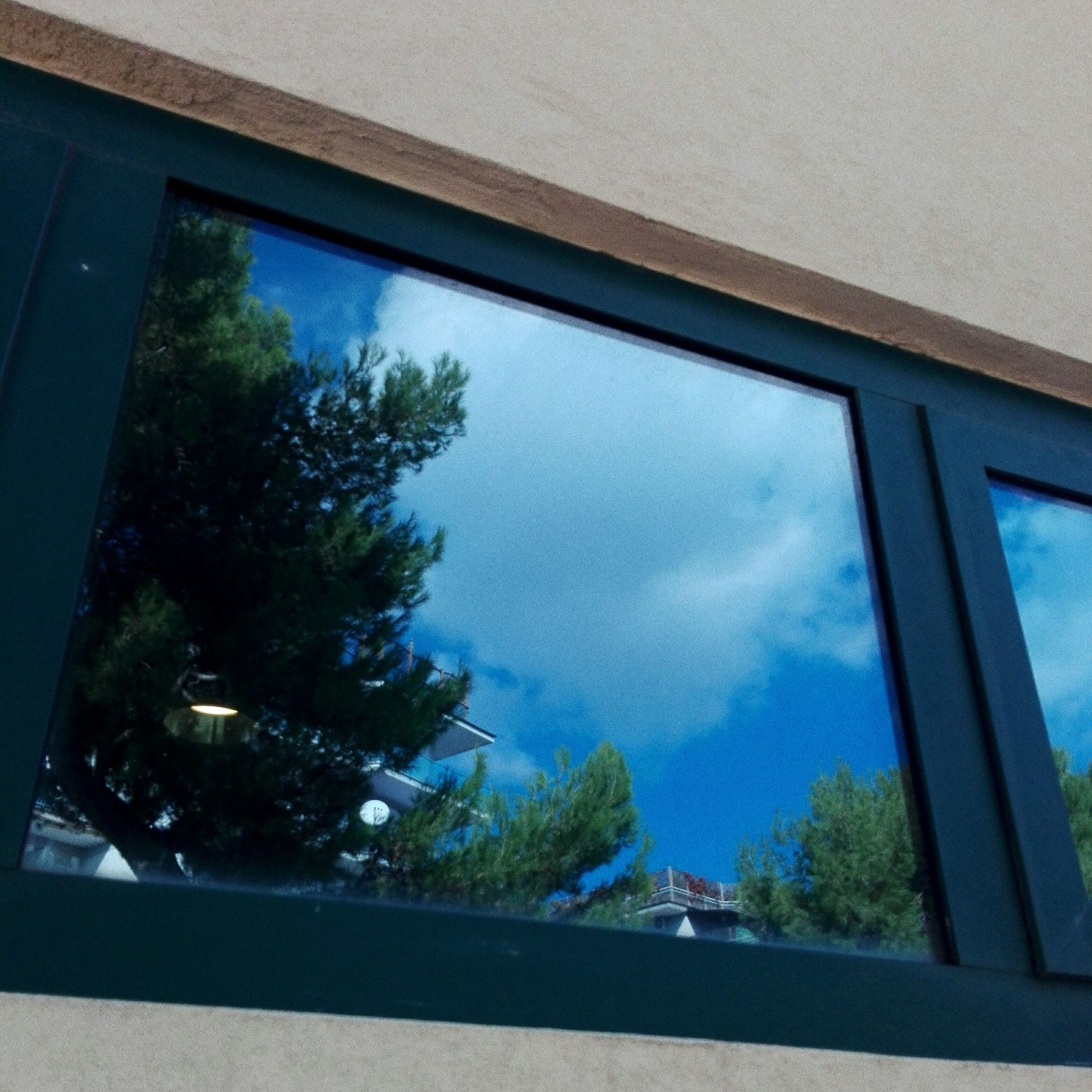 A window with trees reflected in it and a blue sky