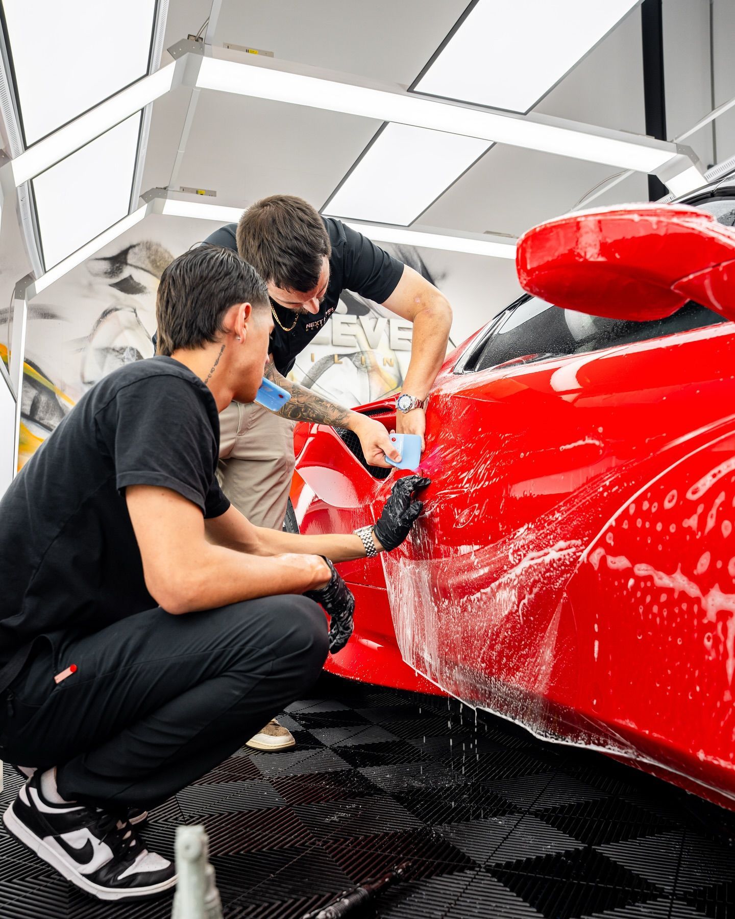 Two men are wrapping a white car in a garage.