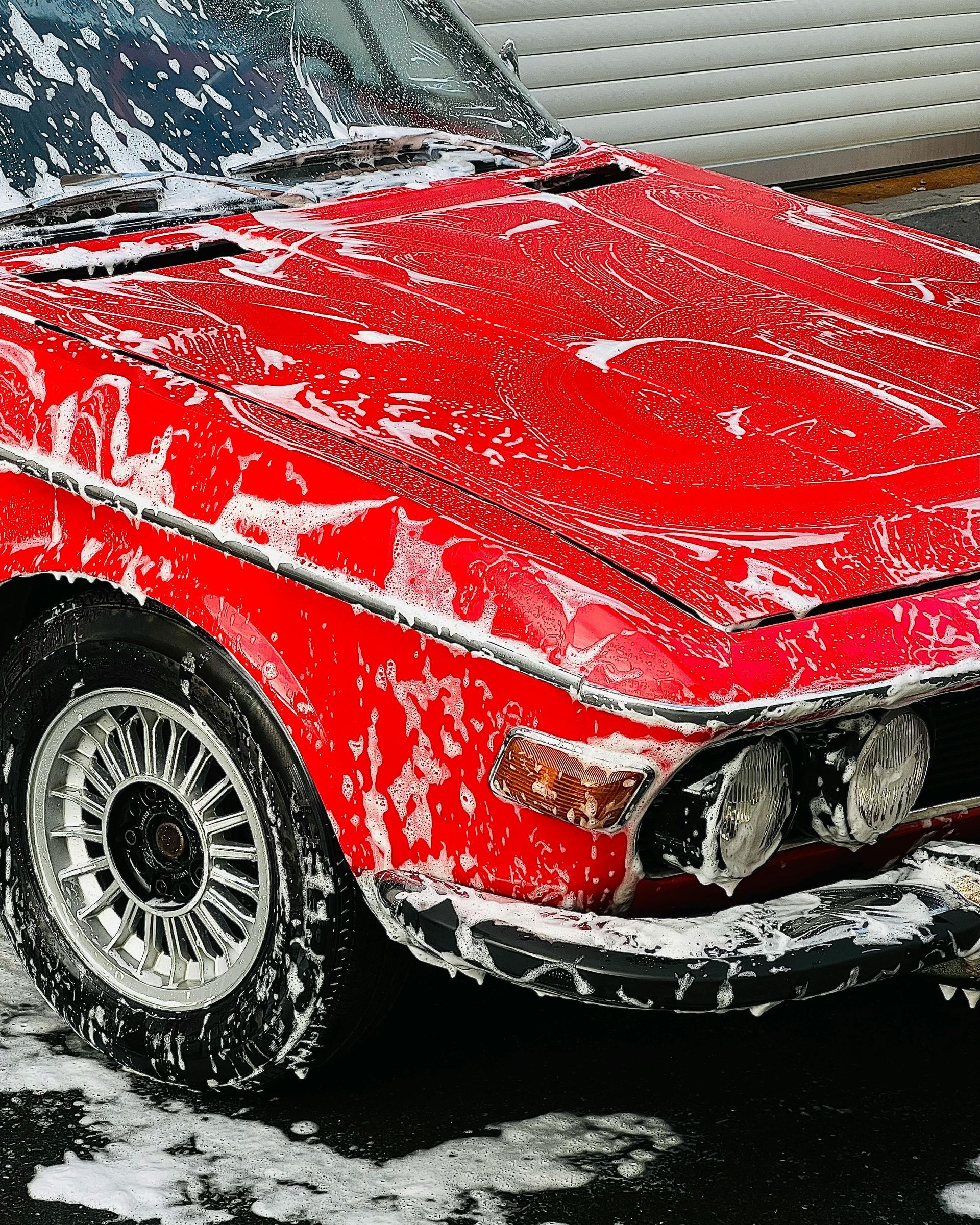 A red car is covered in snow and soap.