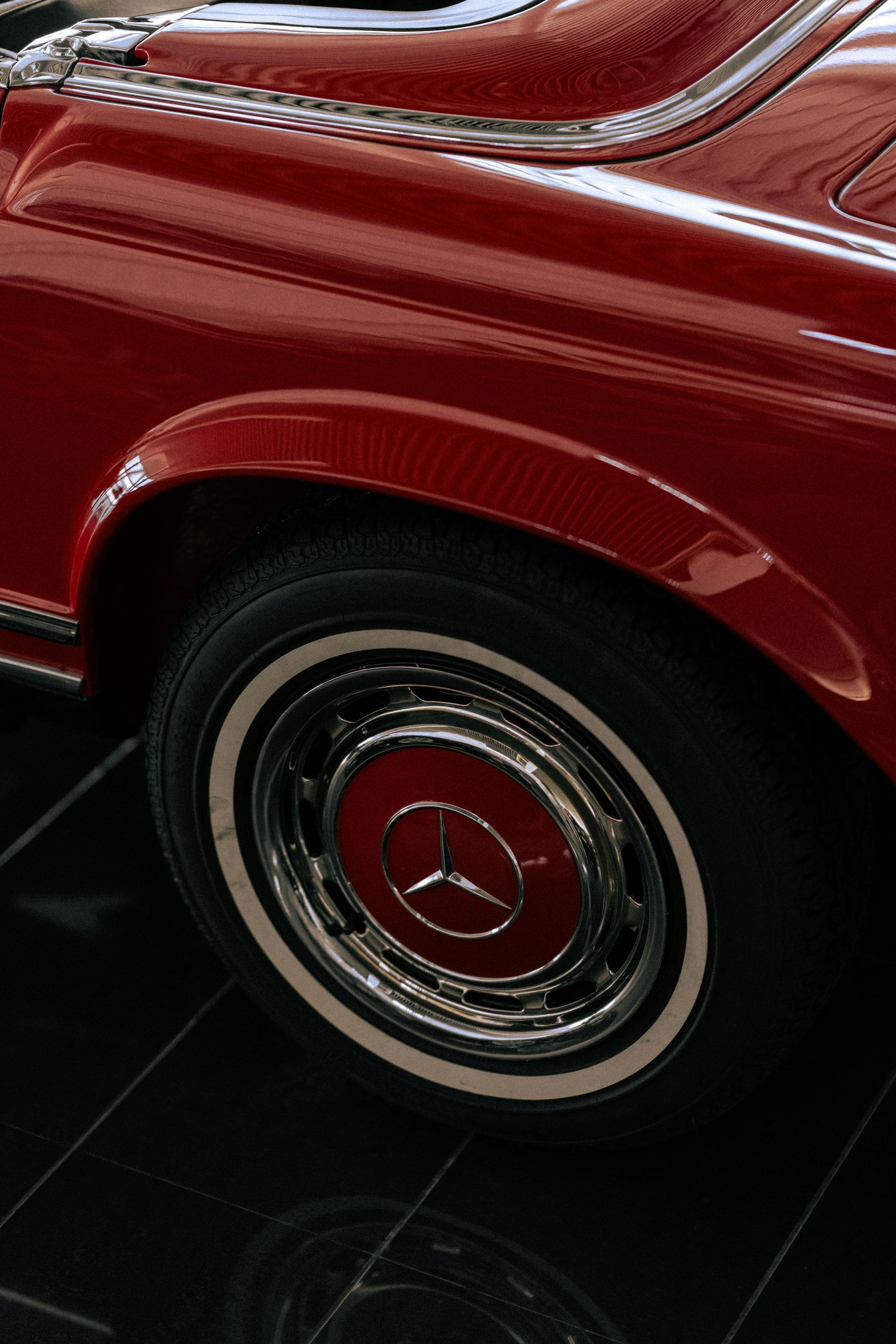 A red mercedes with white tires is parked on a tiled floor.