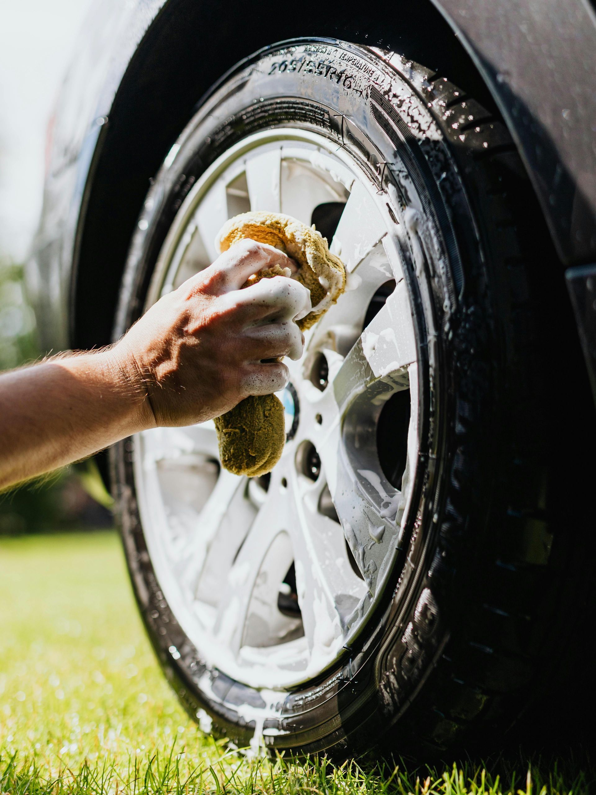 A person is washing a car wheel with a sponge.