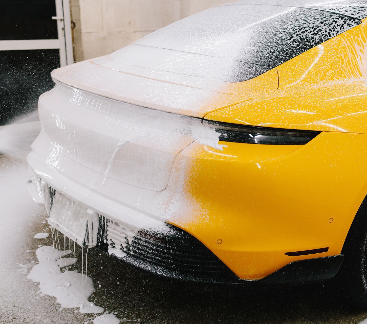 A blue sports car is covered in foam in a parking lot.