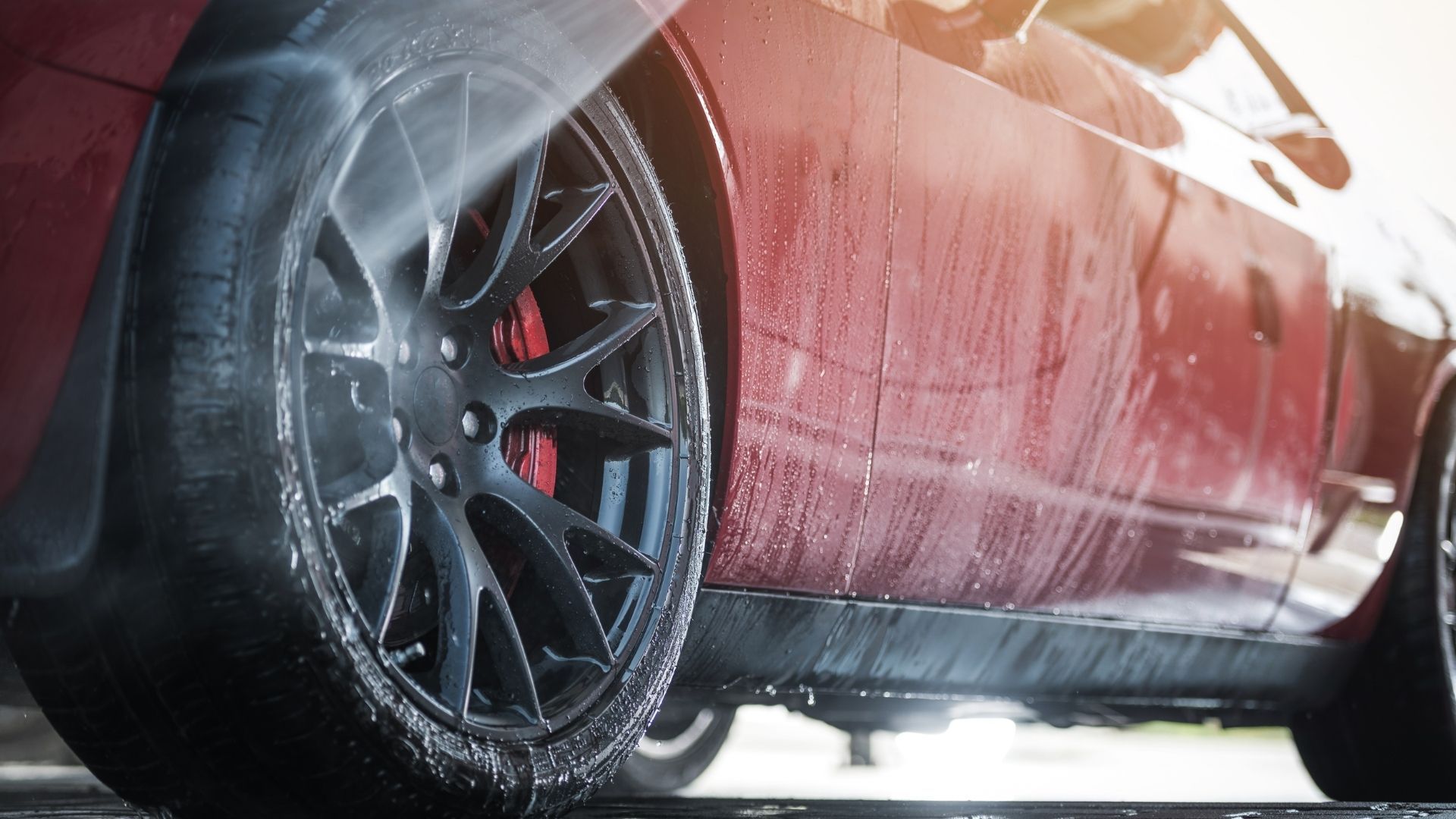 A red car is being washed with a high pressure washer.