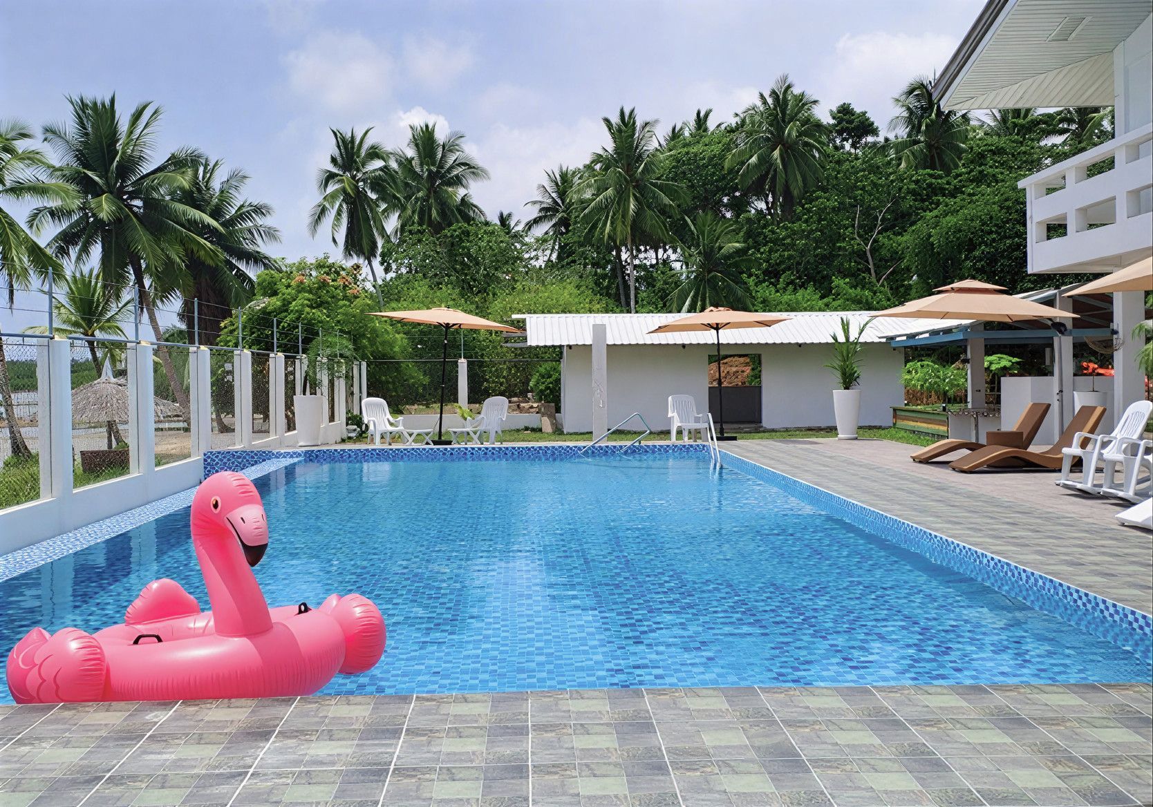 Swimming pool with a pink flamingo float, palm trees, and white buildings.