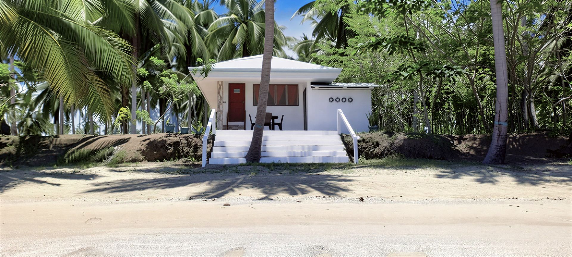White beach bungalow surrounded by palm trees. Steps lead up to the front door.