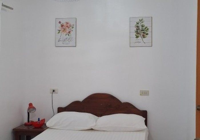 Bedroom with a wooden headboard, two pillows, artwork, and a bedside lamp on a nightstand.