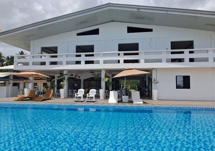A white two-story building with a pool. Lounge chairs and umbrellas surround the pool.