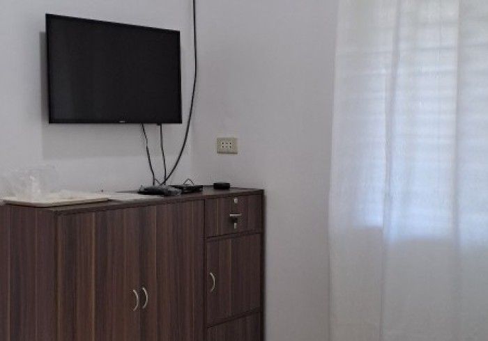 A dark wood cabinet with a TV mounted above it, next to a white curtain.