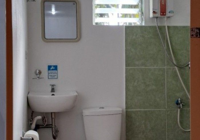 Small bathroom with white walls, accessible sink, toilet, green tiled shower, and mirror.