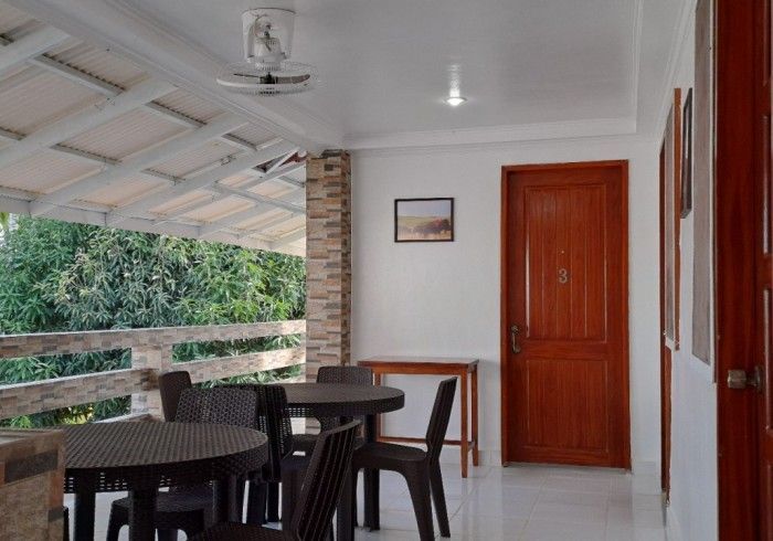 Patio with tables and chairs, white ceiling, brown door, and view of greenery.