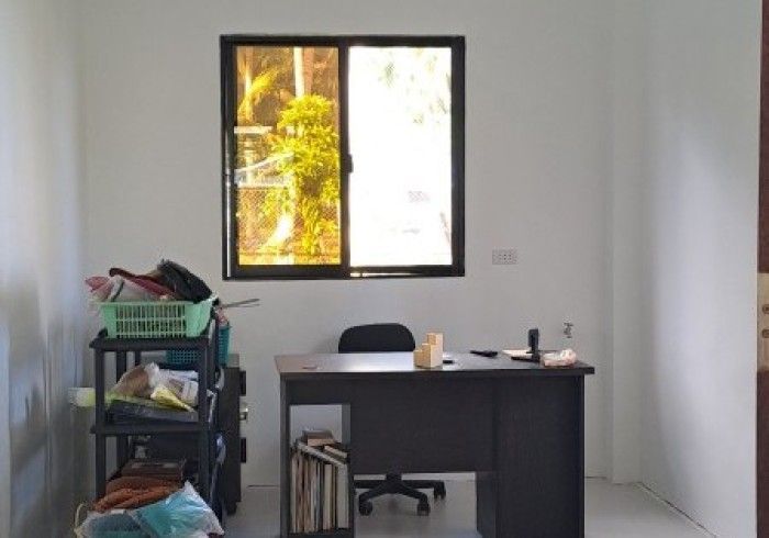A room with a desk, window, and shelves. The window shows trees, and the walls are white.