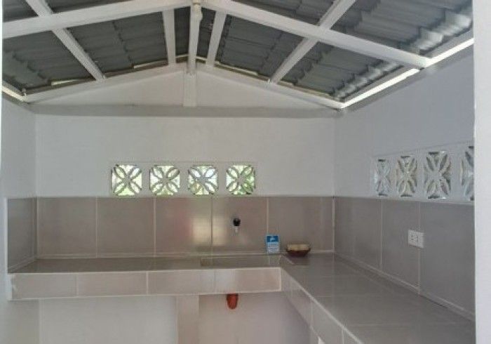 Empty outdoor kitchen with gray countertops, white walls, and a sloped roof.