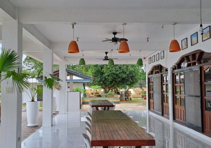 Covered patio with tables, chairs, and hanging lights. View of garden in background.