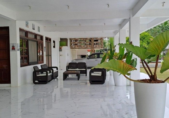 Covered porch with seating area; white pillars, shiny tile floor. Car parked in background. Large plant in foreground.
