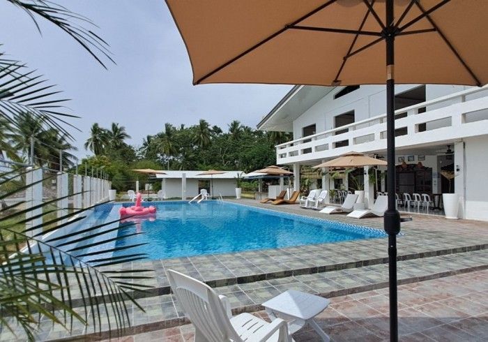 Swimming pool with white house, lounge chairs, and an umbrella on a sunny day.