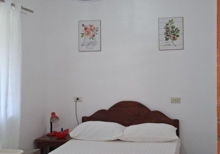 Bedroom with white walls, a bed with white bedding, and two framed floral prints.