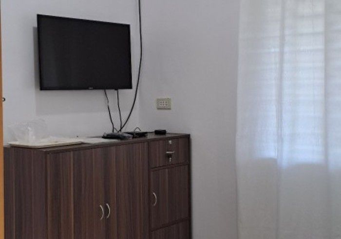 TV mounted on wall above a dark wood cabinet. A window with white curtains is to the right.