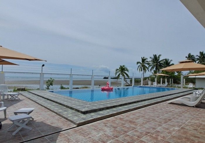 Swimming pool by the beach with a pink flamingo float, palm trees, and umbrellas.