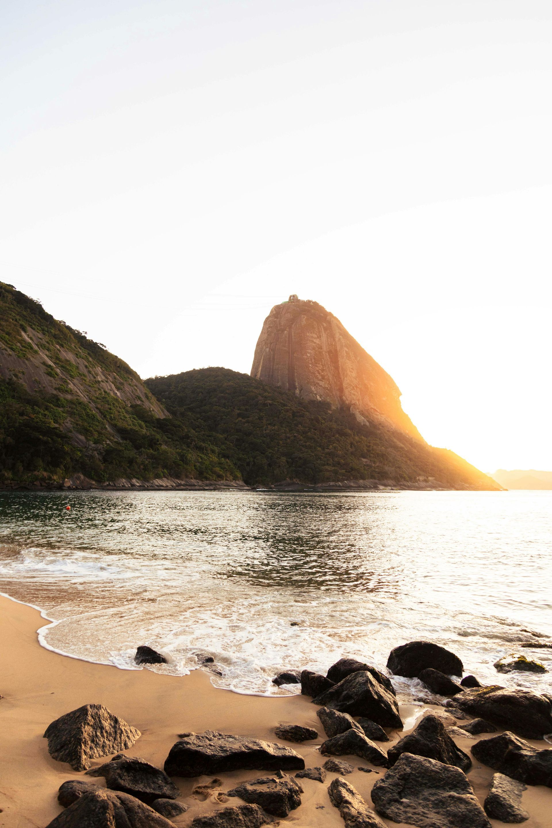 Beach scene with a mountain and setting sun, golden light reflects on the water.