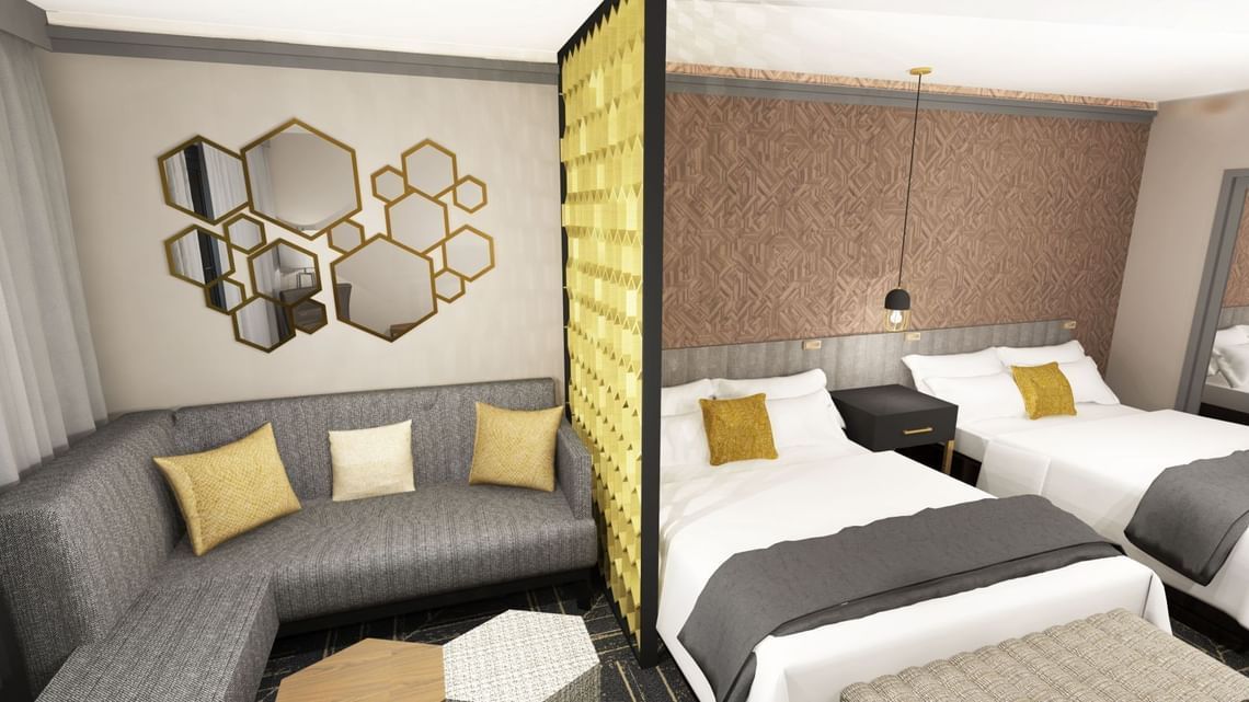 Hotel room with sectional sofa and two beds, separated by a screen. Gold and gray tones.