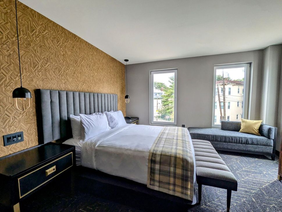 Bedroom with gray upholstered bed, patterned gold wall, two windows, and a chaise lounge.