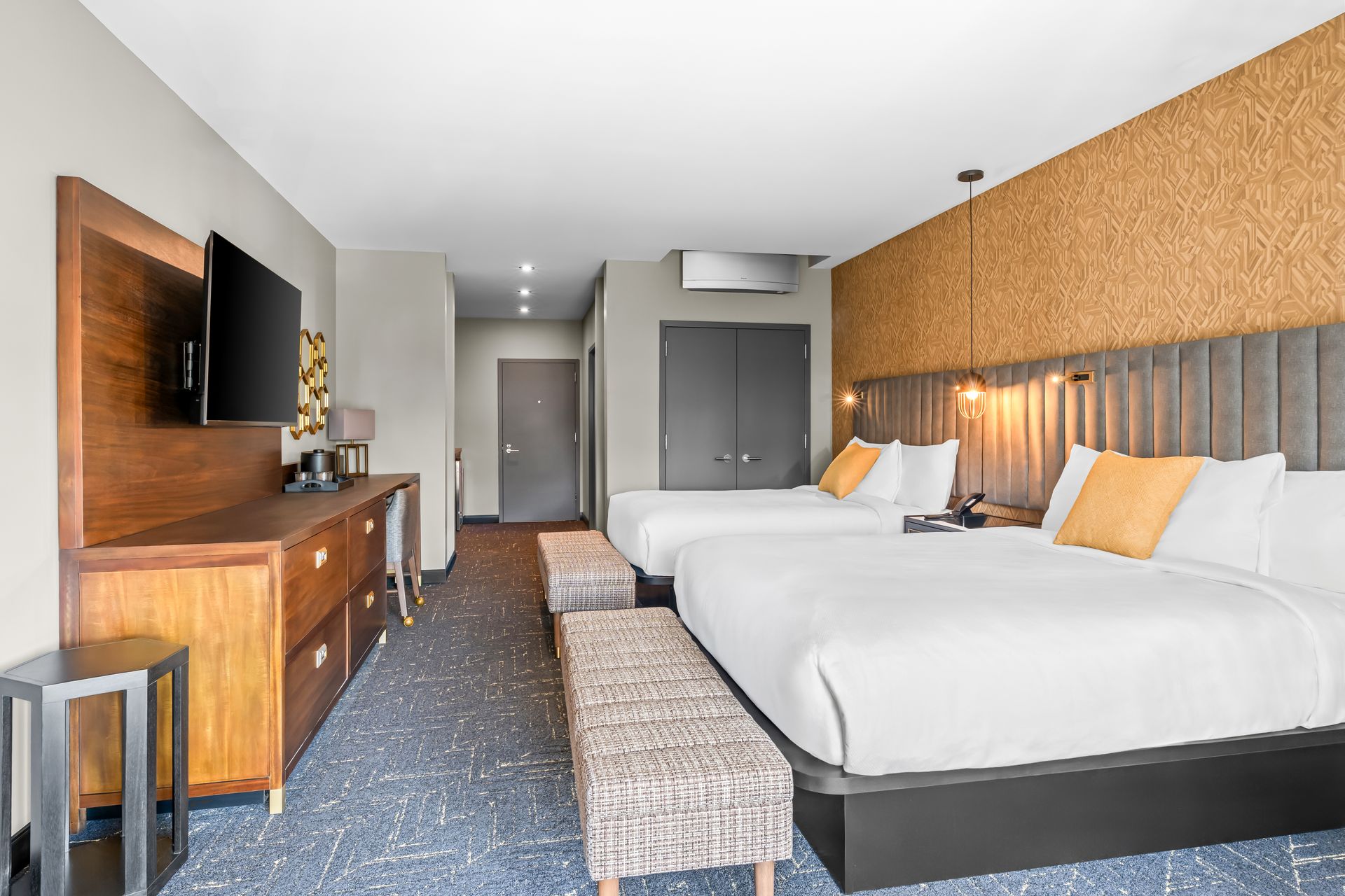 Modern hotel room with two beds, wood-paneled headboard, desk, TV, and a window seat.