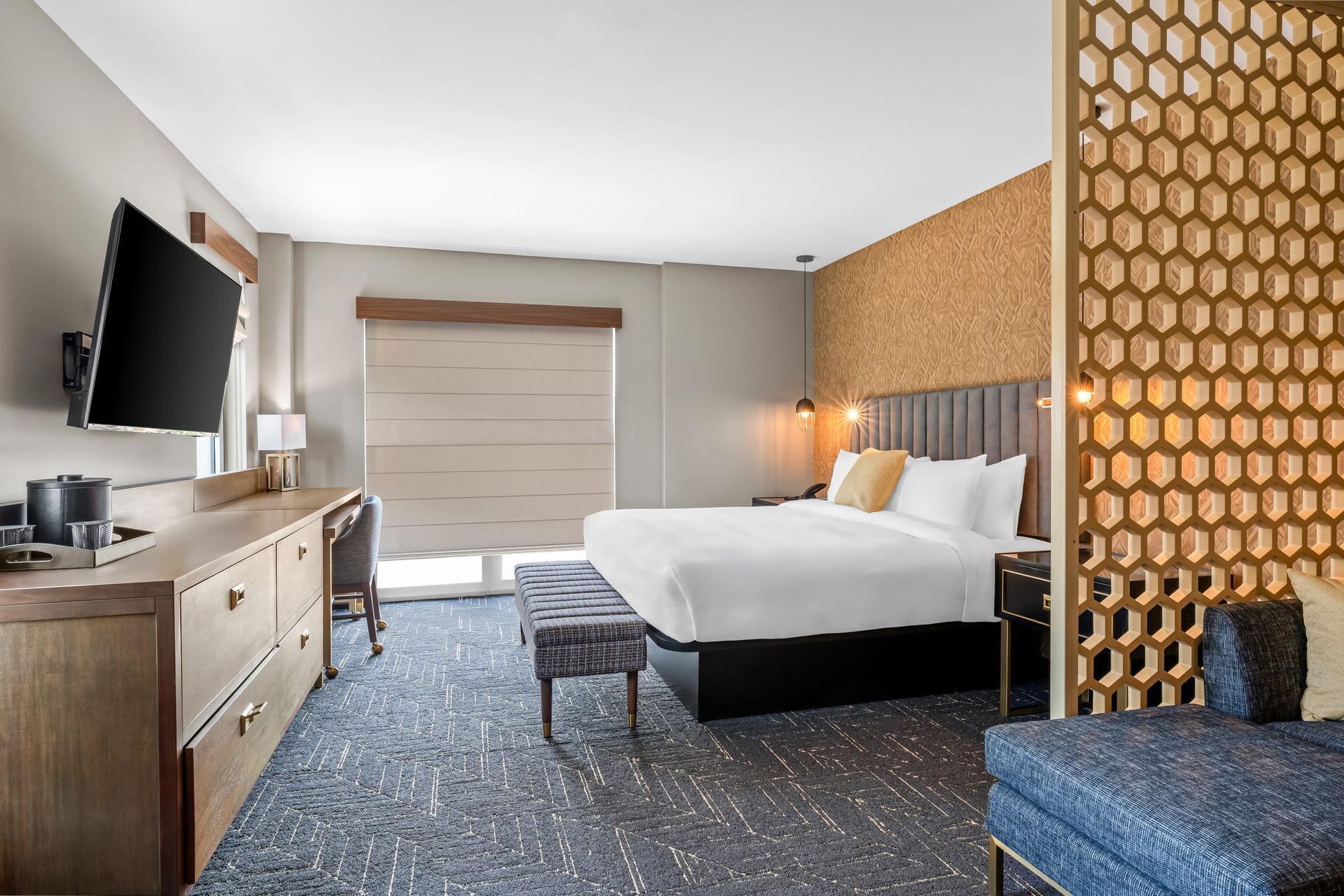 Modern hotel room with a bed, desk, TV, window, and patterned accent wall