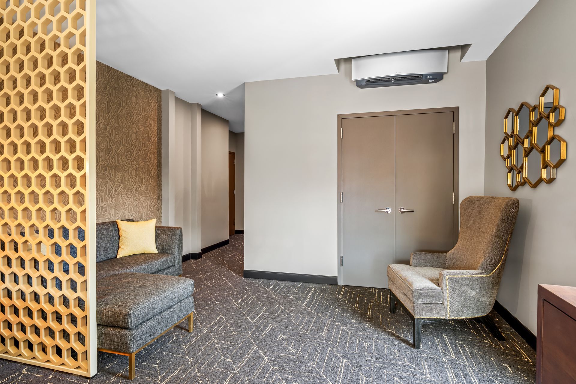 Modern lobby seating area with gray chairs, patterned carpet, and double doors under warm lighting