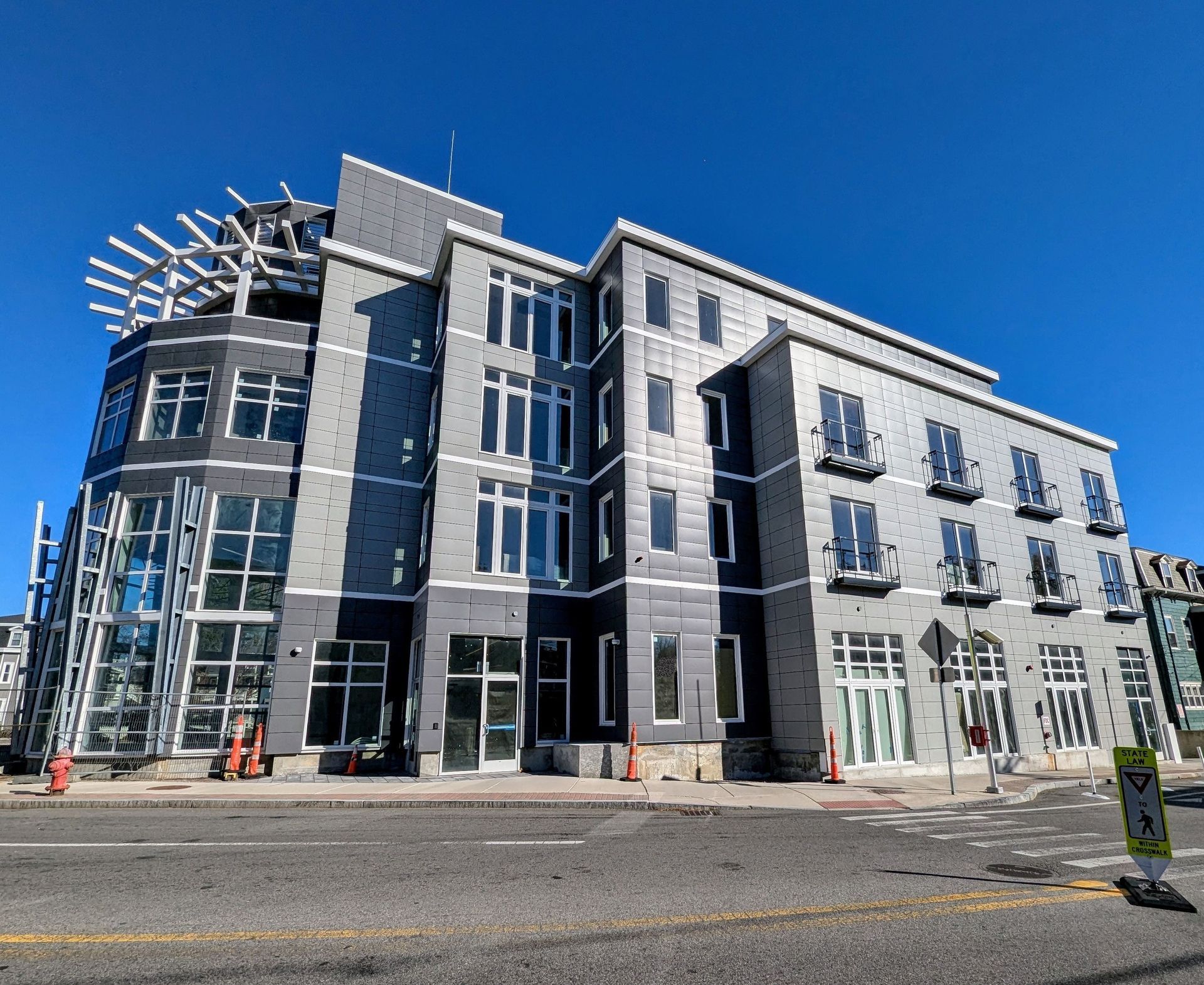 Modern multi-story building with gray siding, large windows, and an open top-level structure under a clear blue sky.