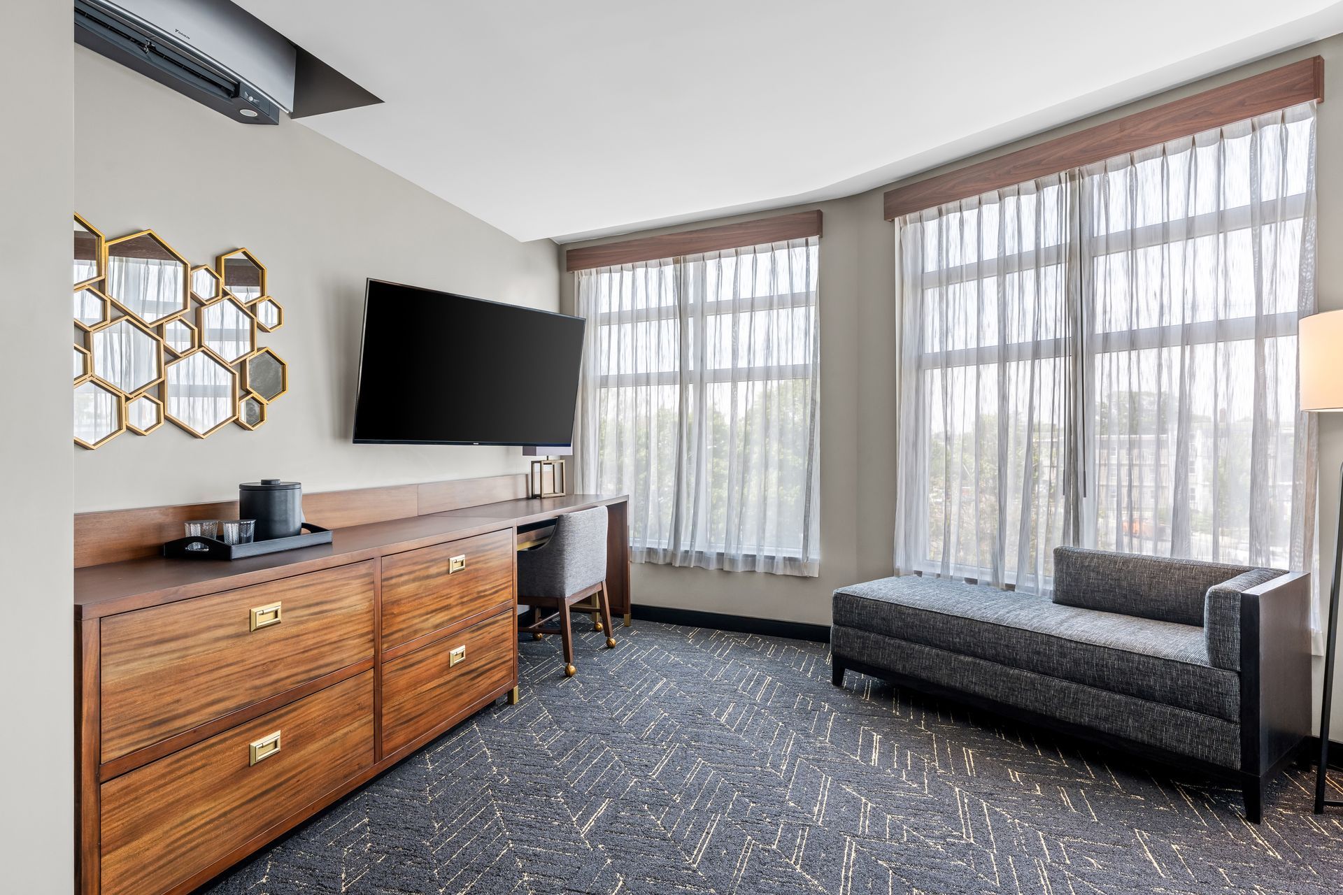 Modern hotel room with dresser, wall-mounted TV, large windows, and a bench