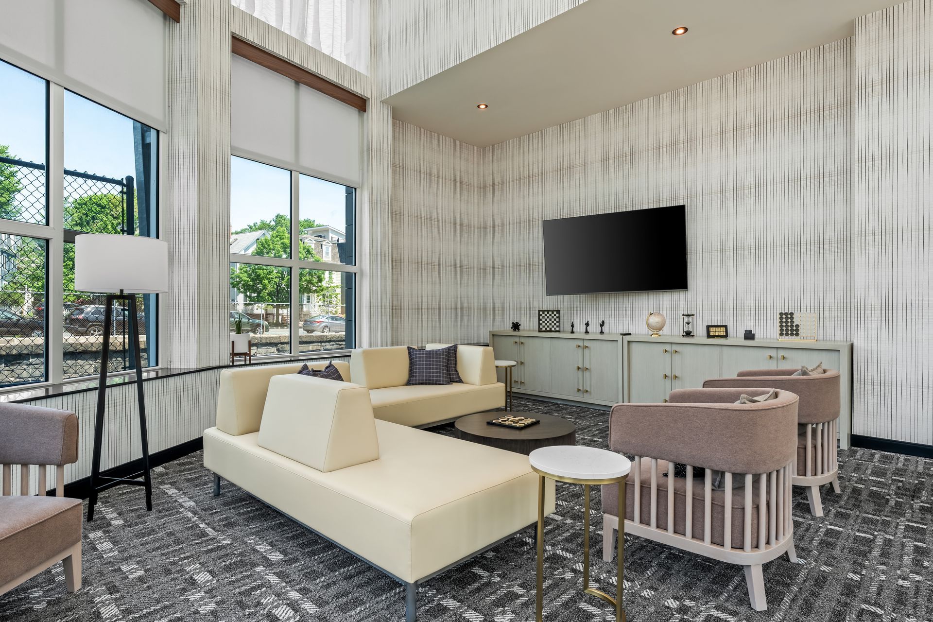 Modern living room with large windows, cream sectional, TV, and pink chairs on a patterned rug