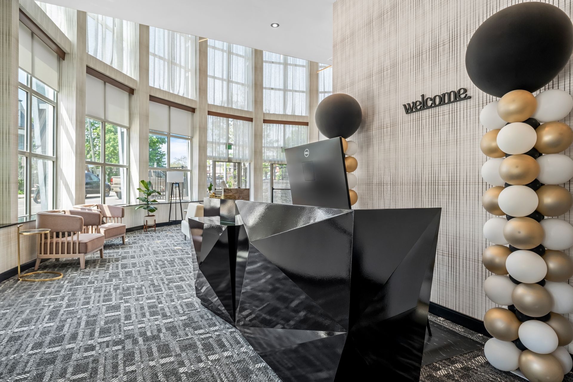 Modern hotel lobby with geometric black reception desk, tall windows, and gold-and-white balloon decor