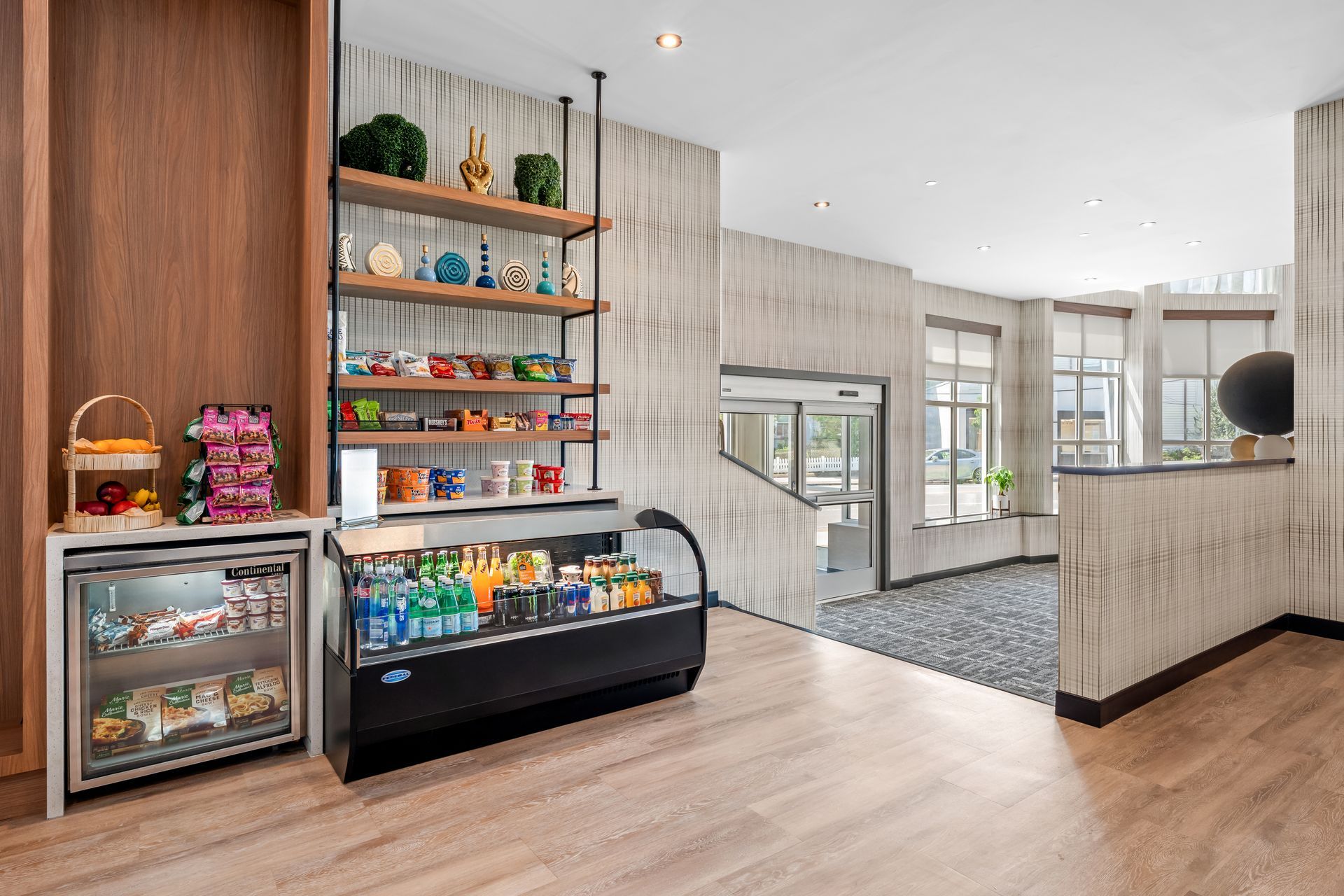 Bright café-style lobby with pastry display cases, shelves of snacks, and large windows