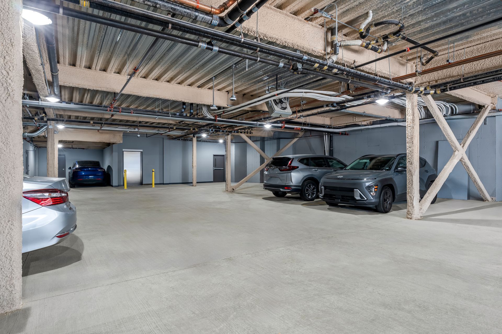 Underground parking garage with several parked cars and exposed beams, open concrete floor.