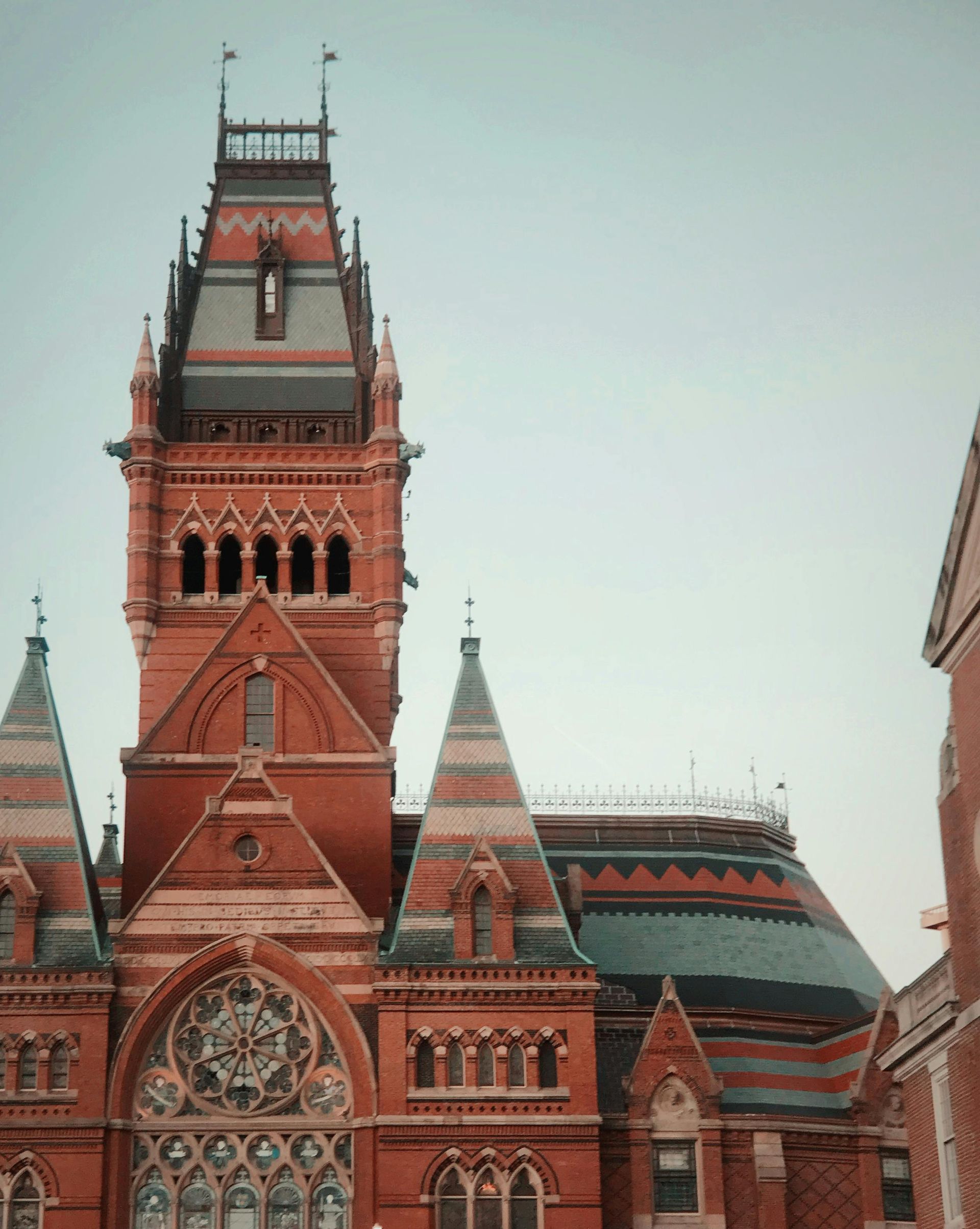Red brick building with a tall tower, multiple turrets, and a light-colored sky.