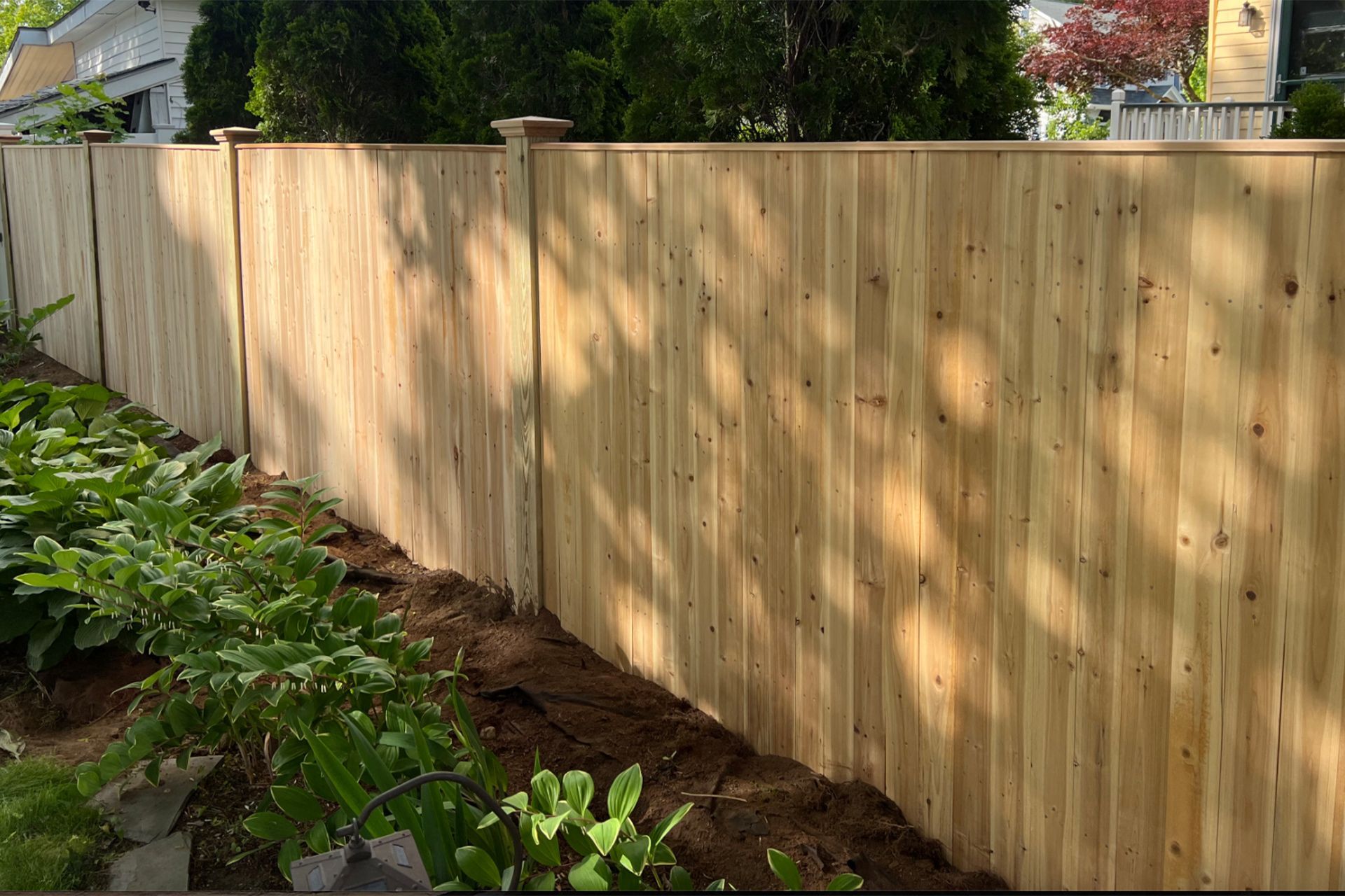 A wooden fence is surrounded by trees and dirt in front of a house.