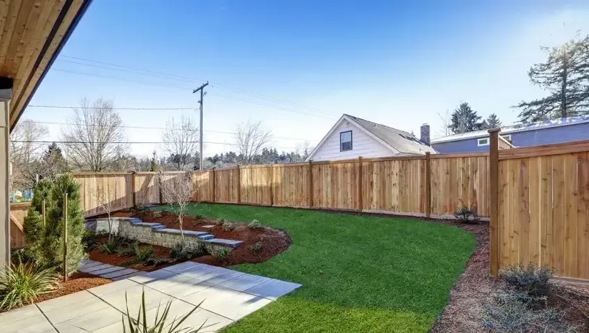 A backyard with a wooden fence and a lush green lawn.