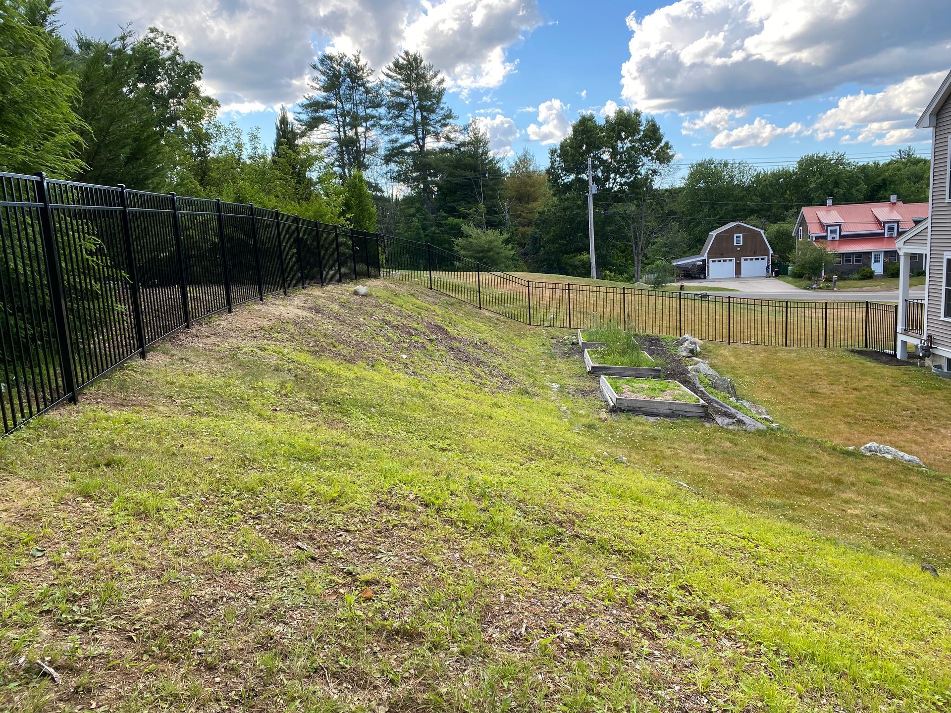 A fence surrounds a grassy field with a house in the background.
